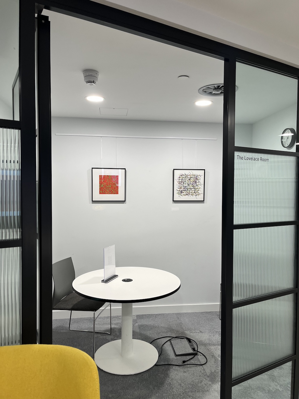 Looking into a small office with a glass door open and two prints on the wall. 